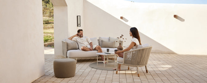 Modernes Lounge-Bereich mit beigem Sofa, weißen Kissen, grauem Stuhl und rundem Tisch.