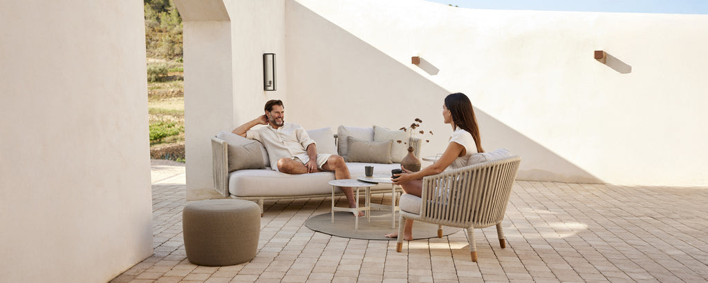 Modernes Lounge-Bereich mit beigem Sofa, weißen Kissen, grauem Stuhl und rundem Tisch.