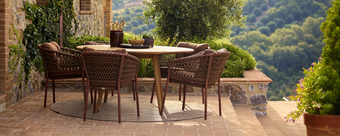 Braune Stühle um einen runden Tisch auf einer malerischen Terrasse mit Grünflächen.