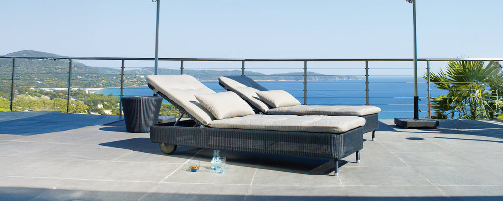 Zwei moderne graue und schwarze Lounge-Stühle auf einer Terrasse mit Blick auf den Ozean.