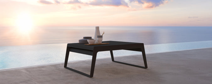 Moderne schwarzer Tisch auf einer Terrasse mit Blick auf den Sonnenuntergang über dem Wasser.