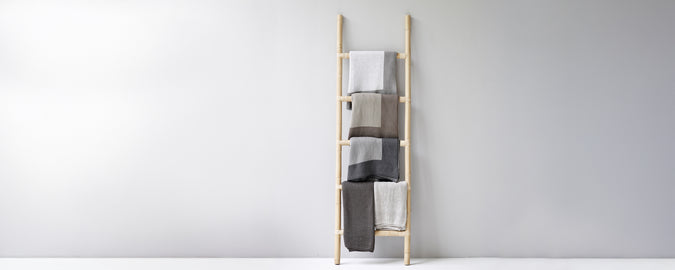 Moderne Handtuchleiter, die beige, graue und weiße Handtücher präsentiert.