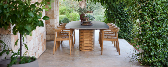 Outdoor-Holztischstühle um einen schwarzen Tisch in einem grünen Garten.