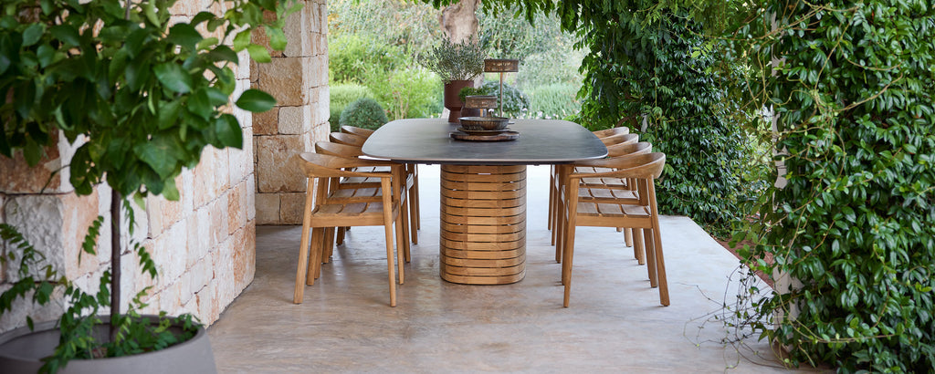 Outdoor-Holztischstühle um einen schwarzen Tisch in einem grünen Garten.