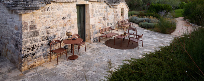 Outdoor seating area with brown chairs and table on a stone patio surrounded by greenery.