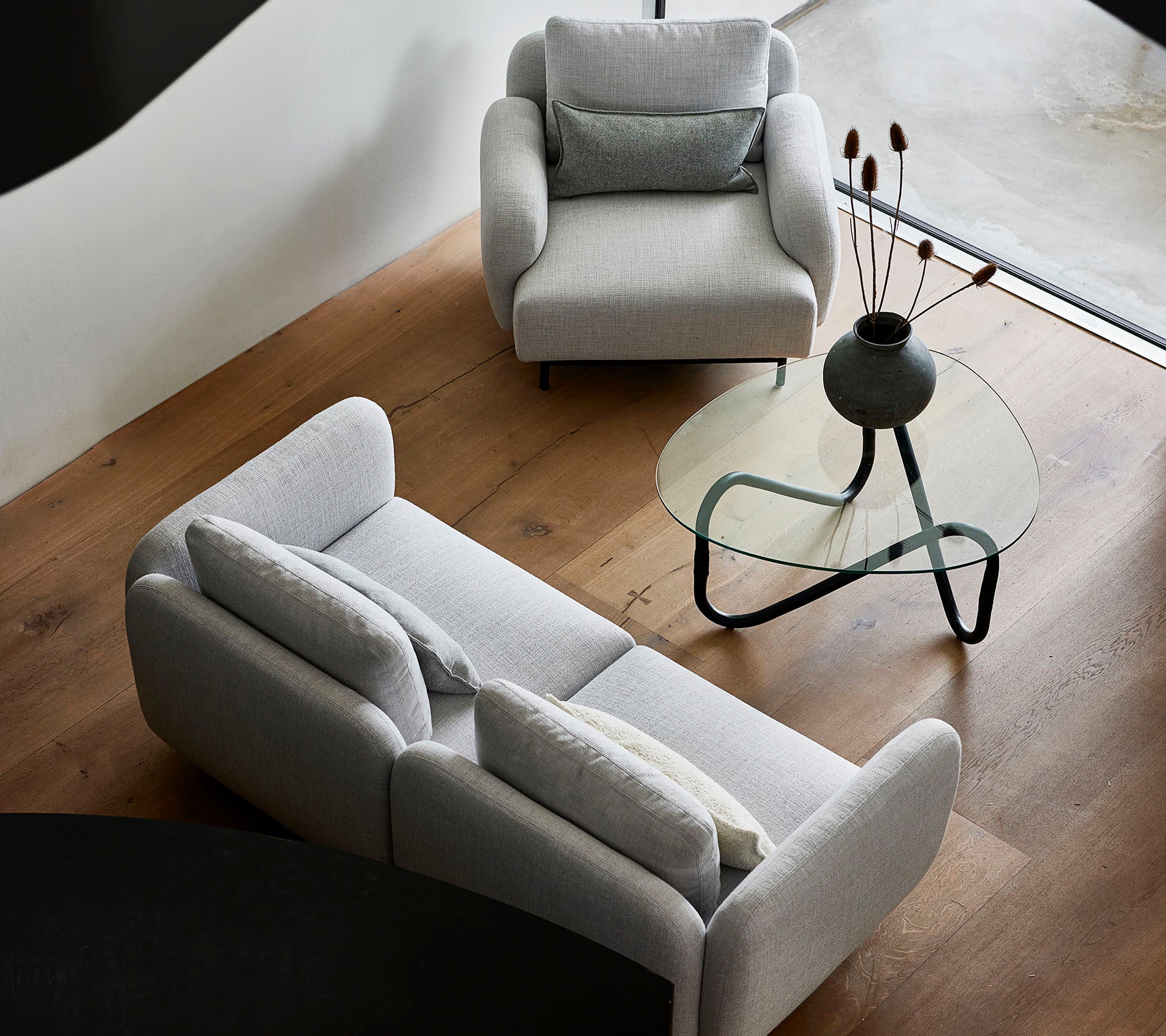Stylische graue Sofas und ein eleganter Glastisch mit dekorativen Elementen auf der Tischplatte, vor einem warmen Holzboden.