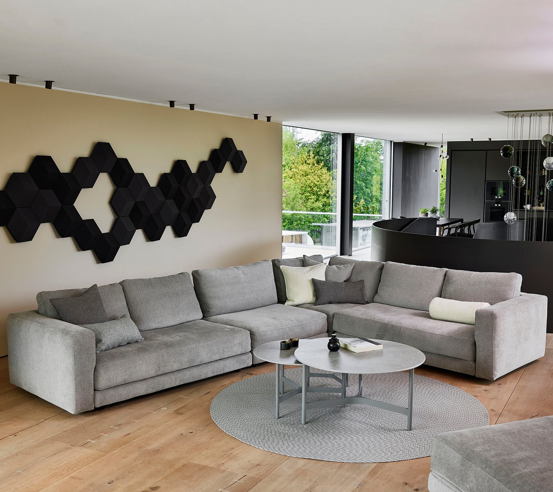Ein modernes graues Ecksofa mit dekorativen Kissen, einem runden Couchtisch und einem strukturierten Wandkunstwerk in Schwarz.