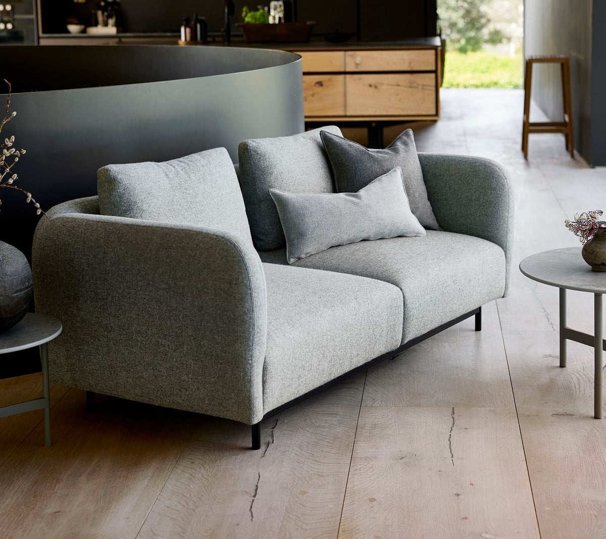 Modernes graues Sofa mit plüschigen Kissen, kombiniert mit einem kleinen runden Tisch, vor einem minimalistischen Hintergrund.