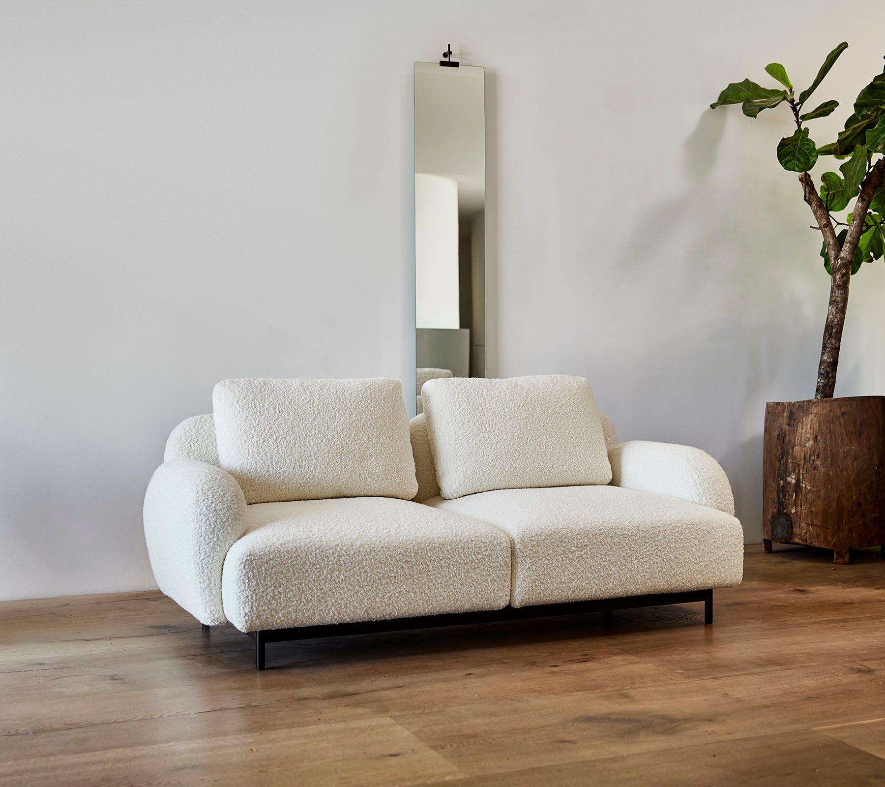 Ein stilvolles weißes Sofa mit plüschigen Kissen, kombiniert mit einem großen Spiegel und einer Topfpflanze in einem modernen Ambiente.