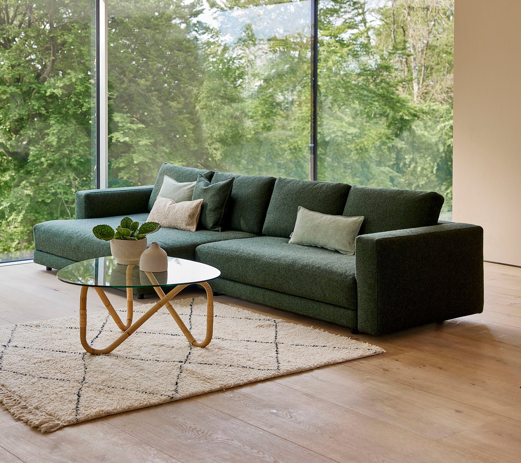 Ein modernes grünes Sofa mit Kissen, begleitet von einem runden Couchtisch und einem dekorativen Teppich, vor dem Hintergrund von Grünpflanzen.