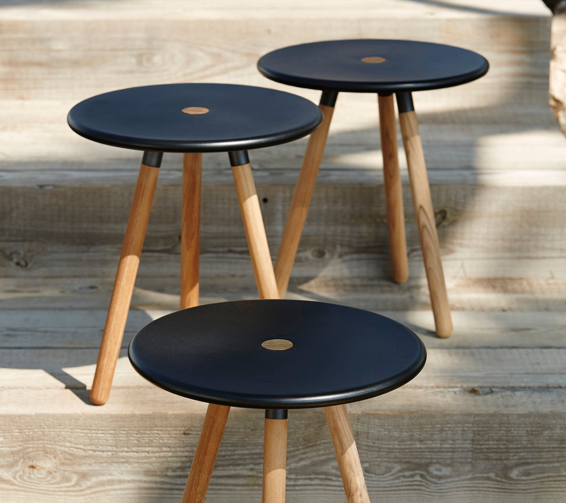 Drei moderne schwarze Hocker mit Holzbeinen auf einer Holzoberfläche.