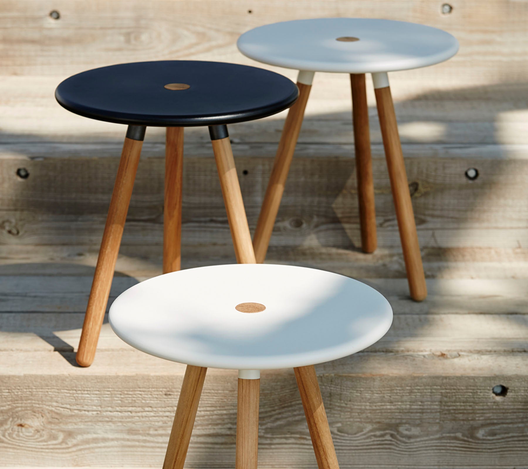 Drei minimalistische Hocker mit runden, schwarz-weißen Oberflächen, die jeweils von Holzbeinen gestützt werden und ein modernes, stilvolles Design präsentieren.