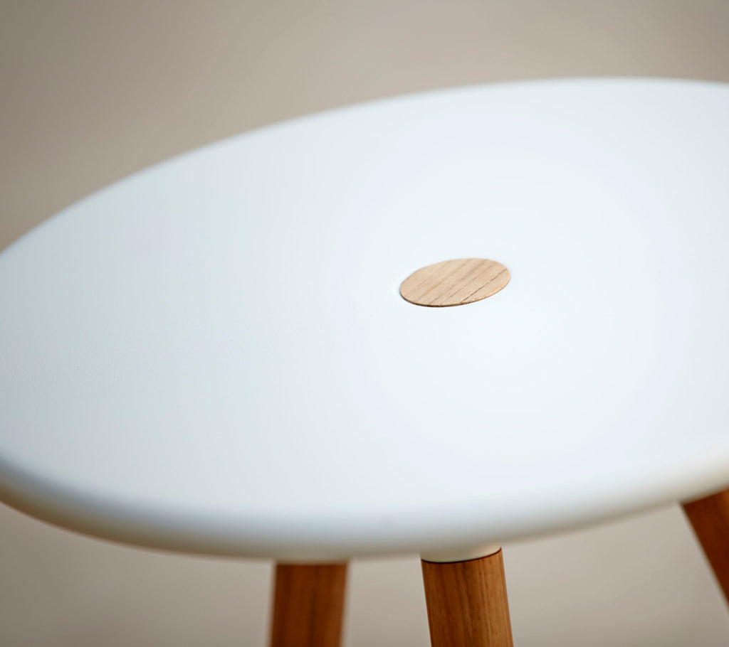 Ein stilvoller Hocker mit einer glatten weißen Oberseite und einem kleinen Holzakzent, gestützt von Holzbeinen. Ideal für moderne Dekoration.