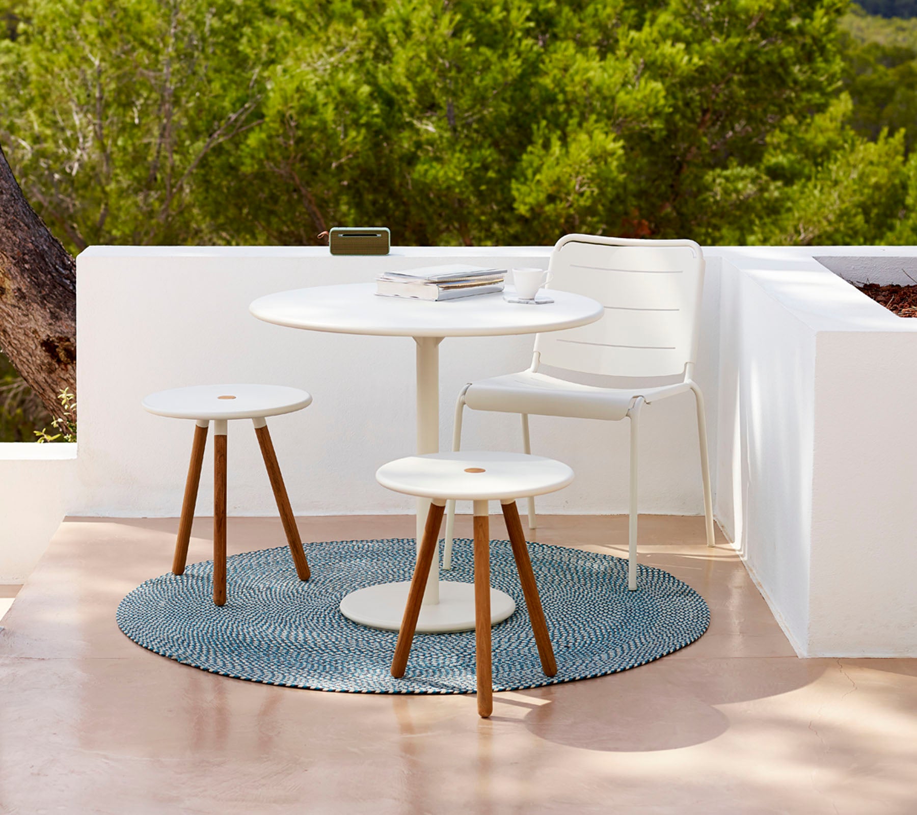 Modernes Gartentischset mit einem runden Tisch, zwei Hockern und einem strukturierten Teppich, umgeben von Grün. Ideal zum Entspannen.