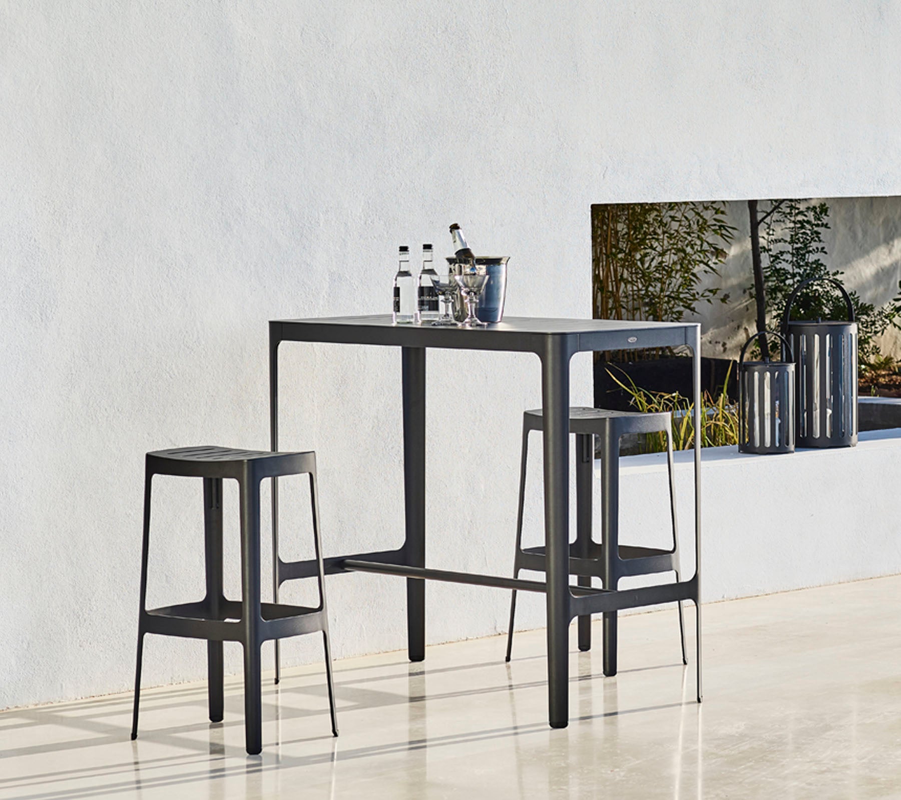 Ein eleganter Tisch mit zwei passenden Hockern, der ein minimalistisches Design aufweist und Flaschen oben darauf platziert sind, vor einem neutralen Hintergrund.