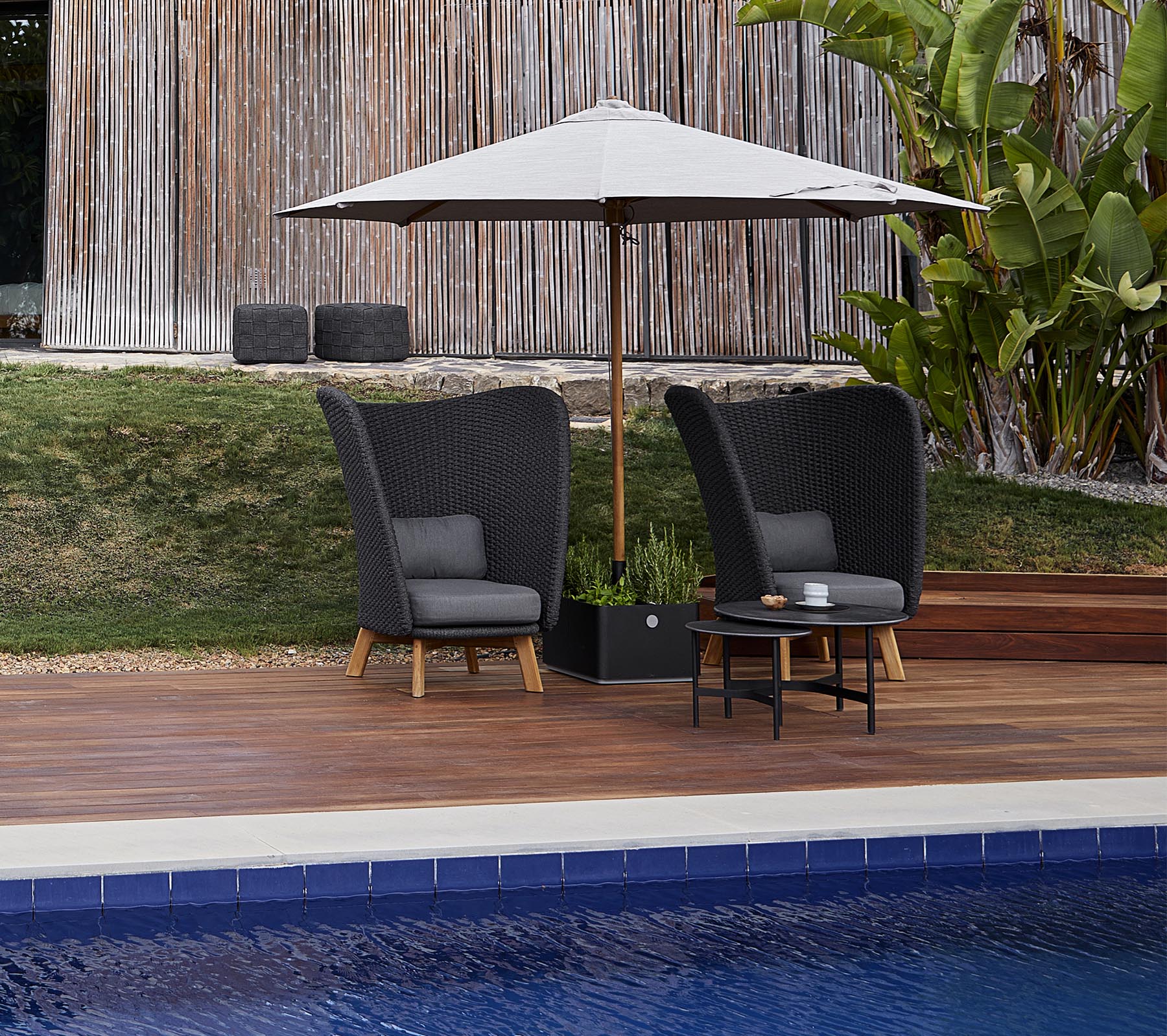 Zwei stilvolle Gartenstühle mit Kissen unter einem großen Schirm, begleitet von einem kleinen Tisch, neben einem Swimmingpool.