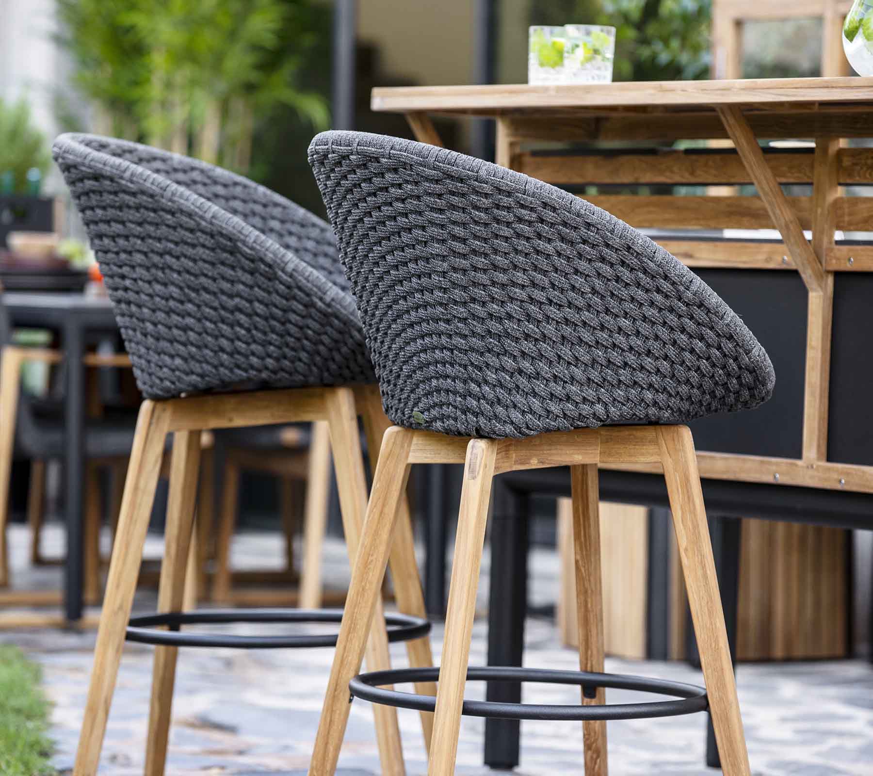 Stilvolle Barhocker mit gewebten grauen Rückenlehnen und Holzbeinen, angeordnet neben einem Holztisch in einem zeitgenössischen Setting.