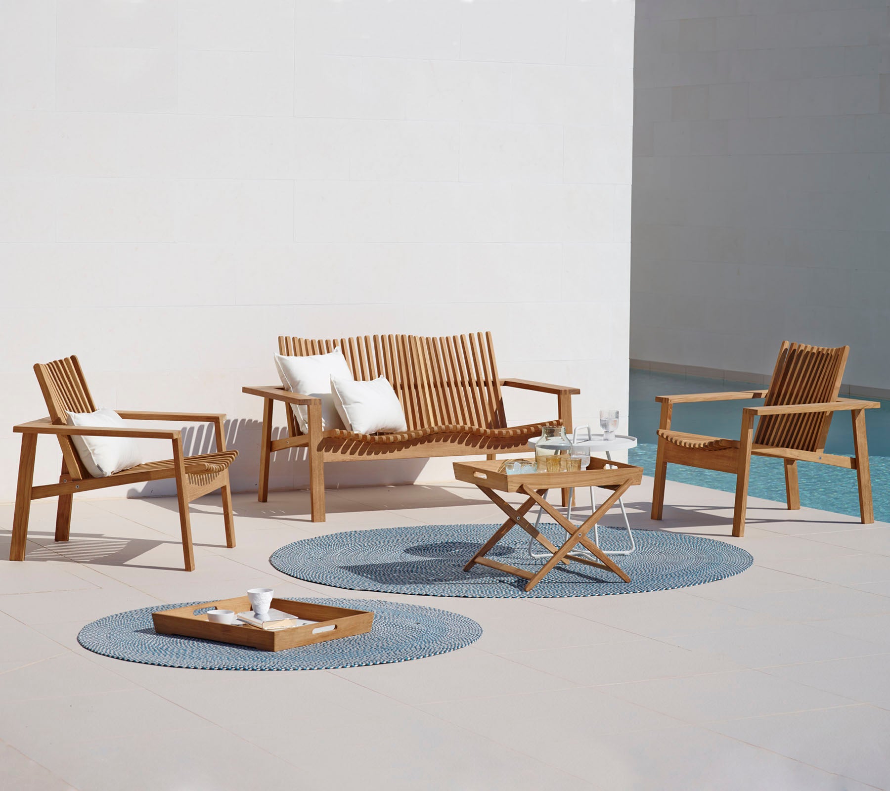 Eine stilvolle Outdoor-Sitzecke mit einem Sofa, zwei Sessel, einem Couchtisch und dekorativen Teppichen. Ideal zur Entspannung.