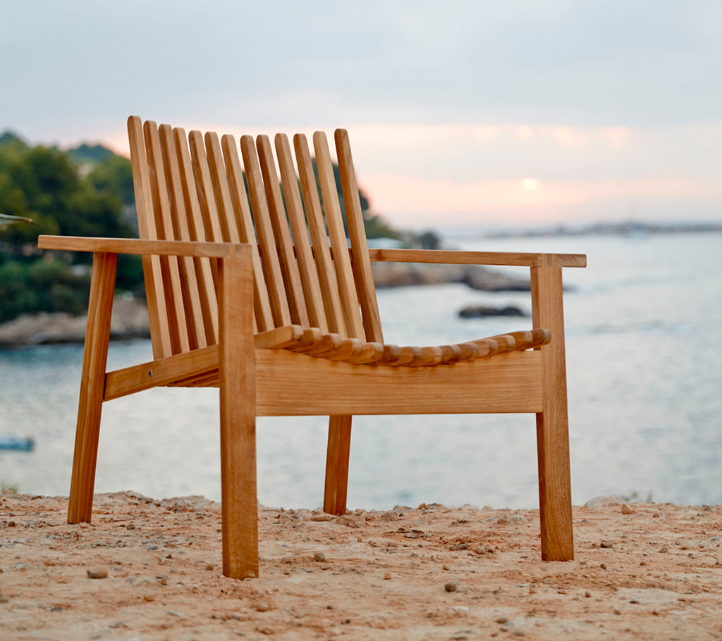 Ein Holzstuhl mit latten Rückenlehne und Sitz, nahe dem Wasser positioniert, der eine natürliche und ruhige Umgebung zeigt.