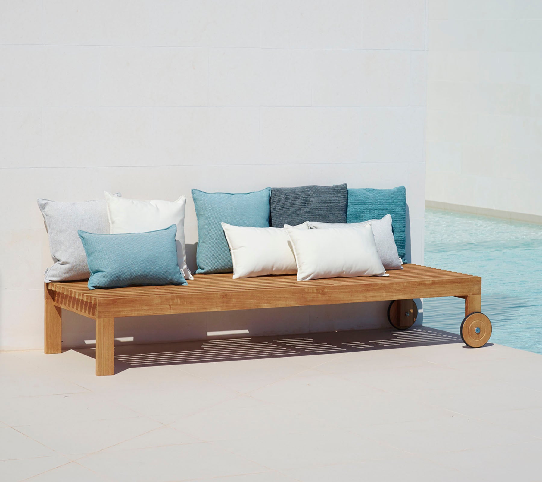 Holz-Loungesofa mit einfachem Design, ausgestattet mit Kissen in Blau- und Weißtönen, neben einem Pool positioniert.