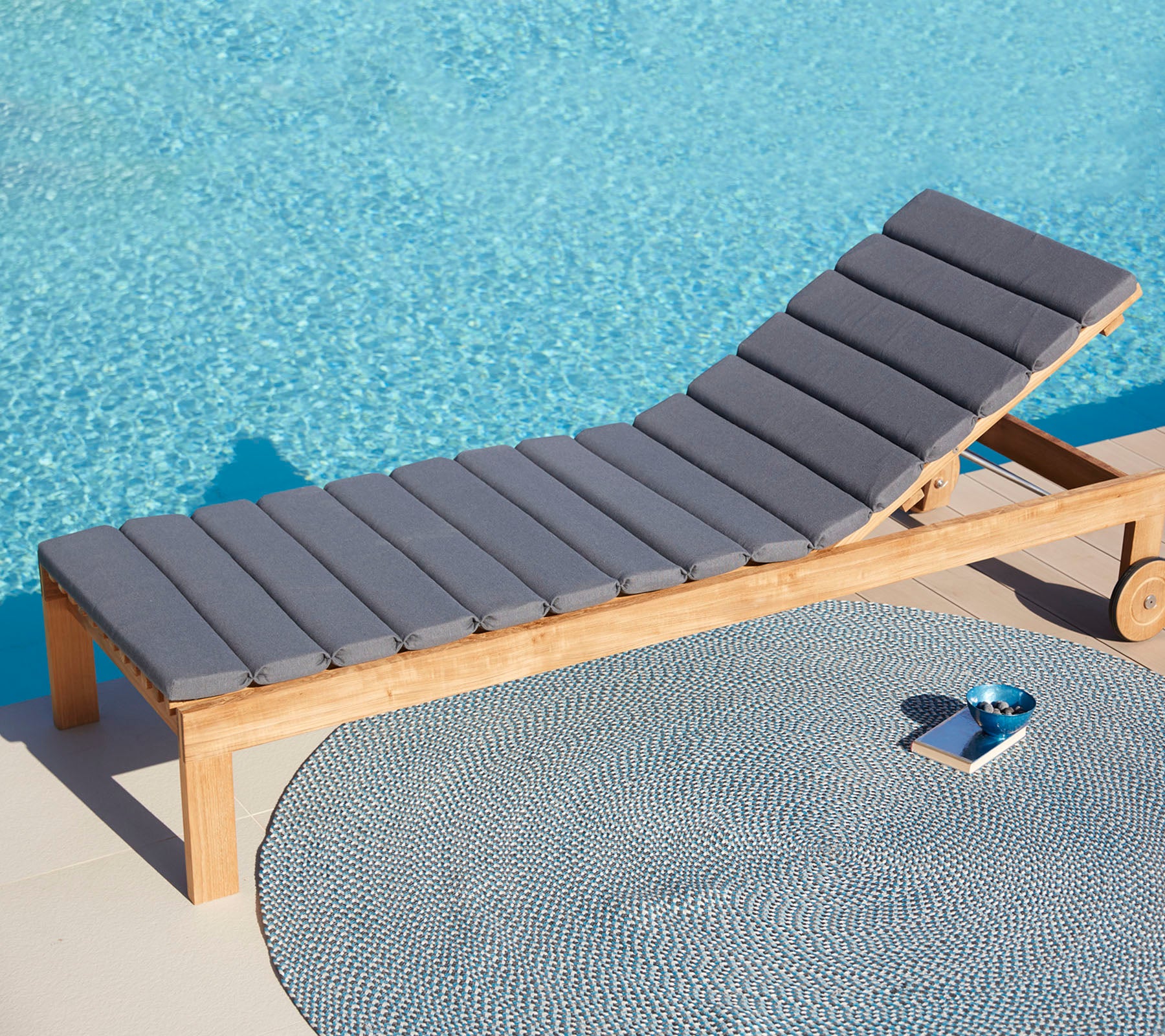 Bequ chair gula Widersekomst, der ein runder Teppich und ein kleiner Tablett, mit einer ruhigen blauen Wasseroberfläche im Hintergrund.