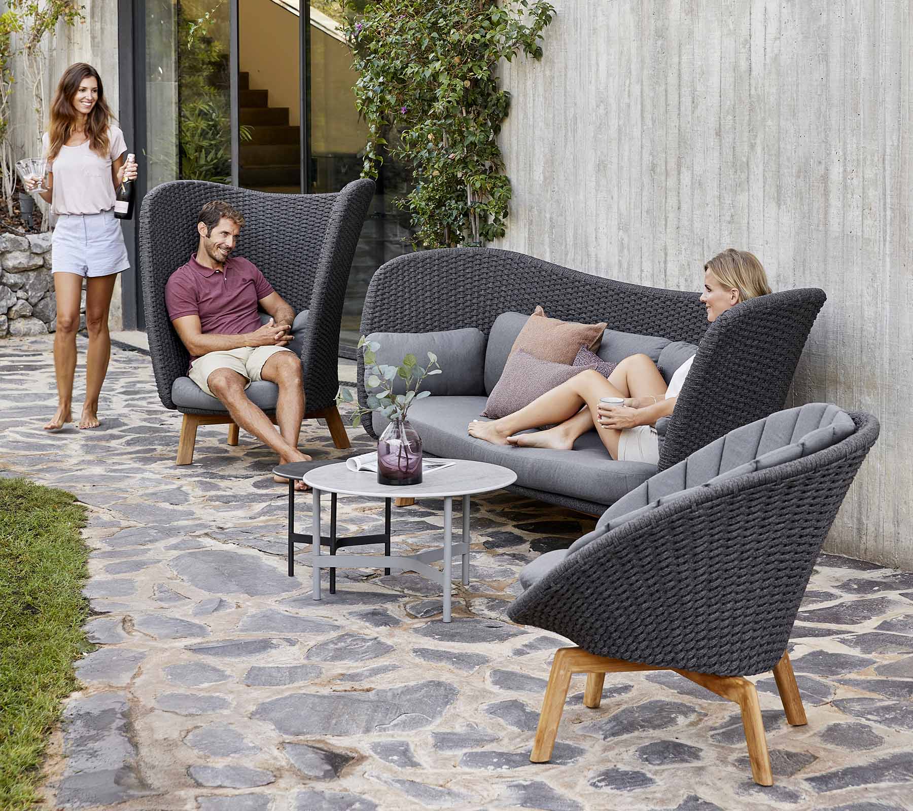 Stilvolle Außensitzanordnung mit einer geschwungenen Couch und Stühlen, mit einem kleinen Tisch, umgeben von Grünpflanzen.