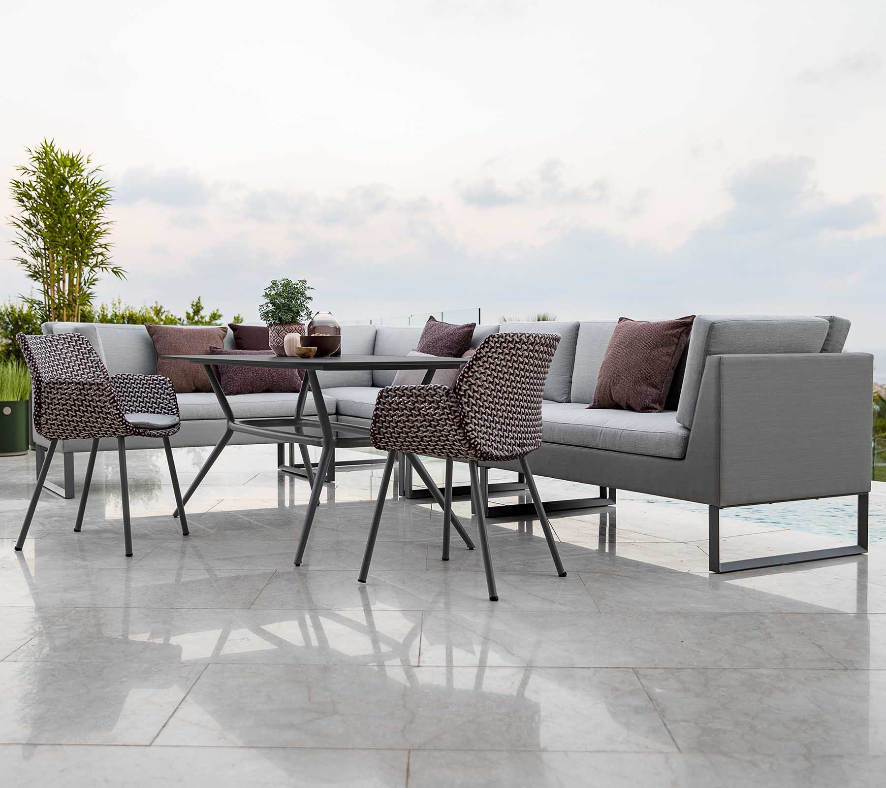 Moderne Outdoor-Sitzanordnung mit einem modularen Sofa mit Kissen, einem Glastisch und stilvollen Stühlen.