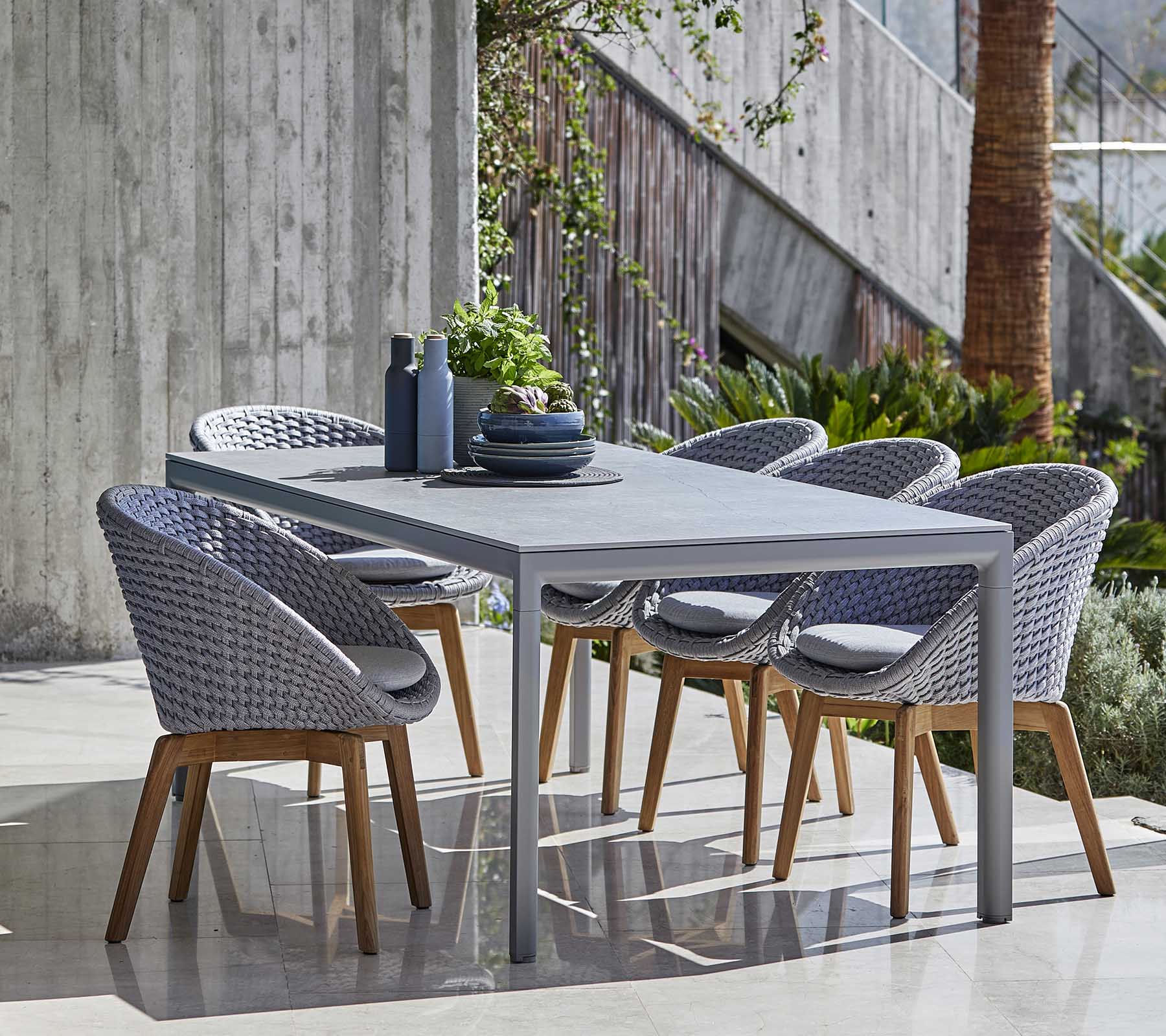 Modernes Esszimmer-Set mit einem grauen Tisch und geflochtenen Stühlen mit Holzbeinen, ordentlich arrangiert mit dekorativen Gegenständen auf dem Tisch.