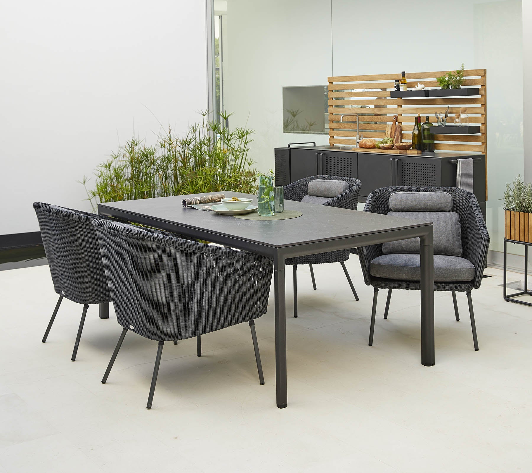 Modernes Esszimmer-Set für den Außenbereich mit einem eleganten Tisch und vier stilvollen Stühlen mit bequemen Kissen, umgeben von Grün.