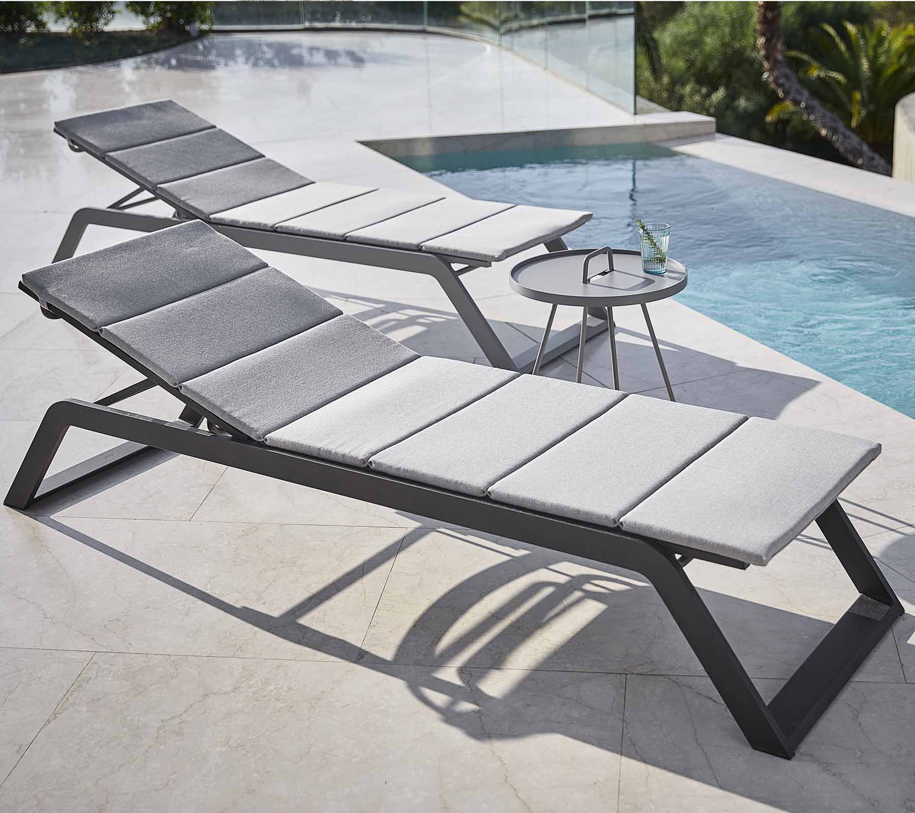 Zwei stilvolle Loungesessel mit grauen Kissen stehen neben einem Pool, begleitet von einem kleinen Beistelltisch mit einem Getränk.