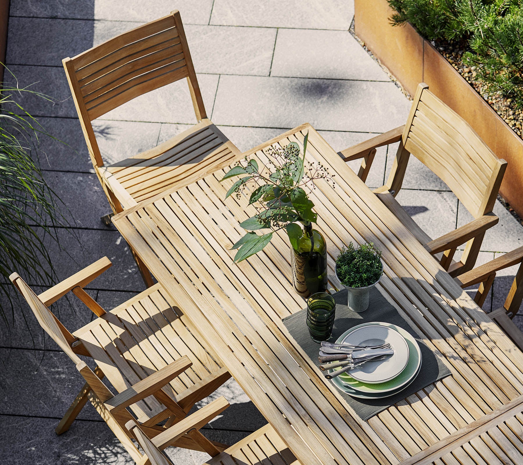 Holztischset mit rechteckigem Tisch und Klappstühlen, geschmückt mit Grünpflanzen und Geschirr für eine einladende Atmosphäre.