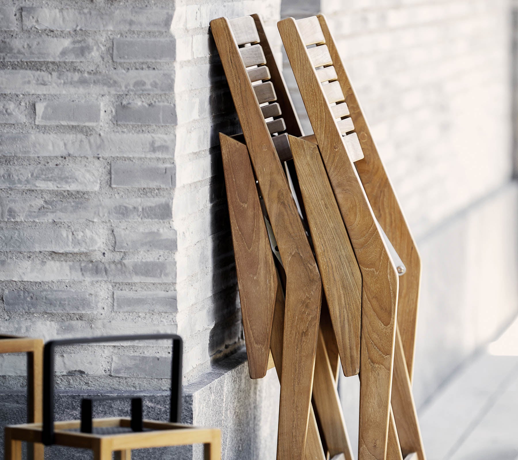 Drei Holzständer mit einem eleganten Design, die an einer strukturierten Wand lehnen, begleitet von einem einfachen, stilvollen Stuhl im Vordergrund.