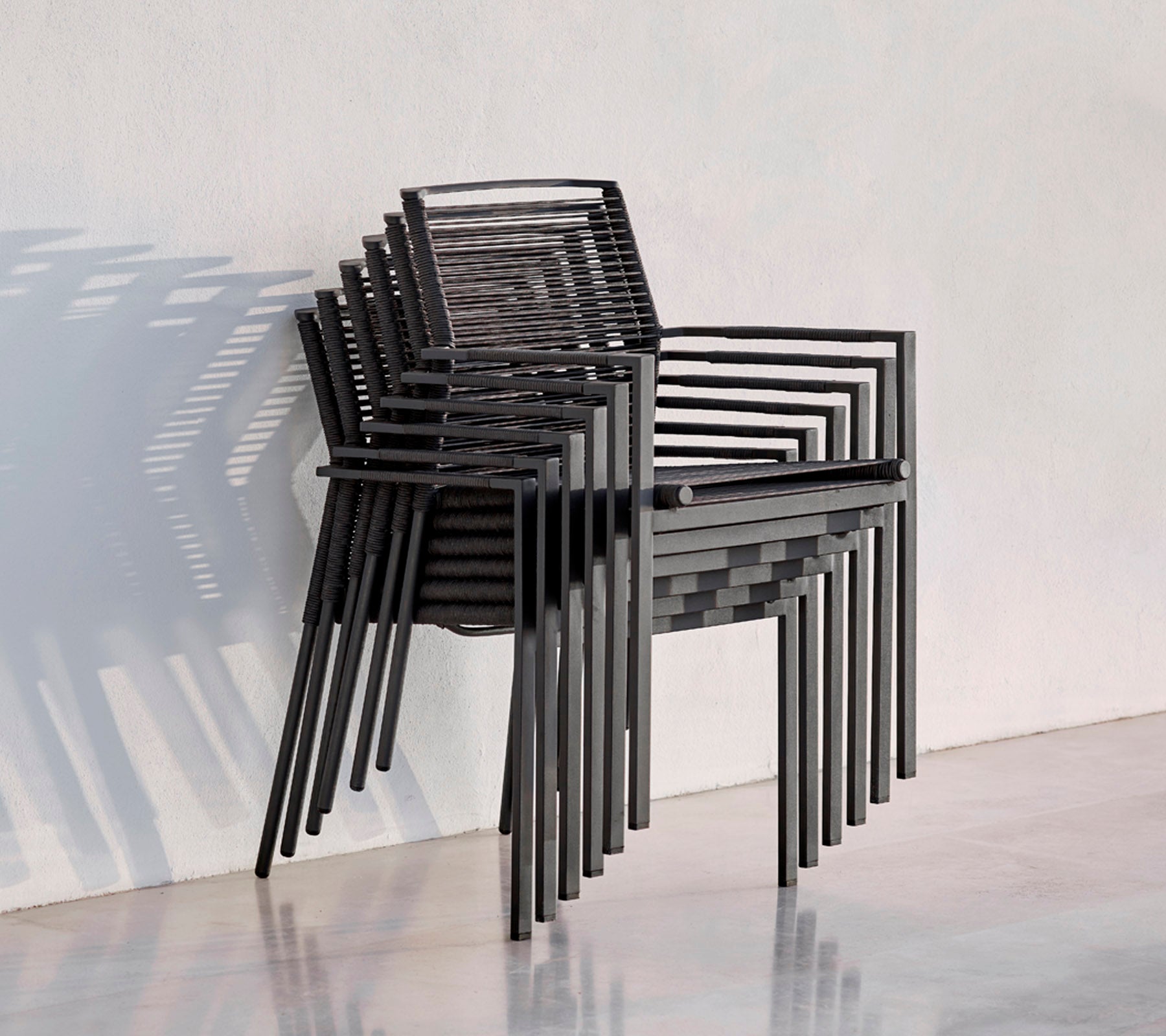 Ein Stapel moderner schwarzer Stühle mit schlankem Design, der Schatten auf einen hellen Hintergrund wirft.