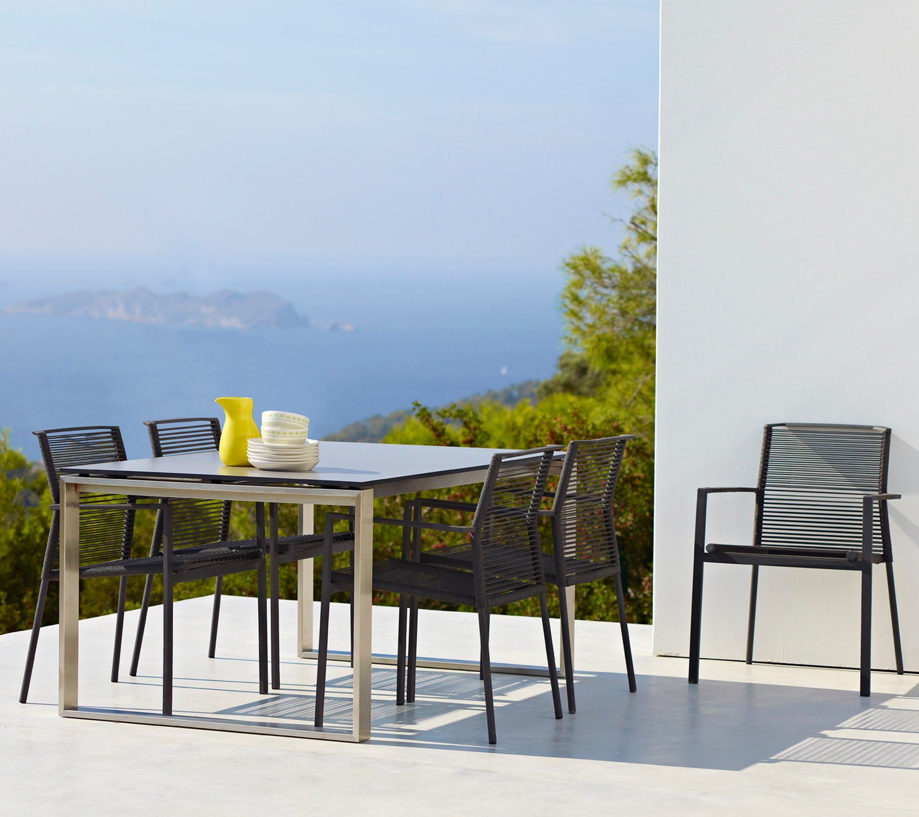 Ein stilvolles Esszimmer-Set mit einem rechteckigen Tisch, sechs Stühlen und einer Vase mit gelben Blumen, vor einer malerischen Kulisse.
