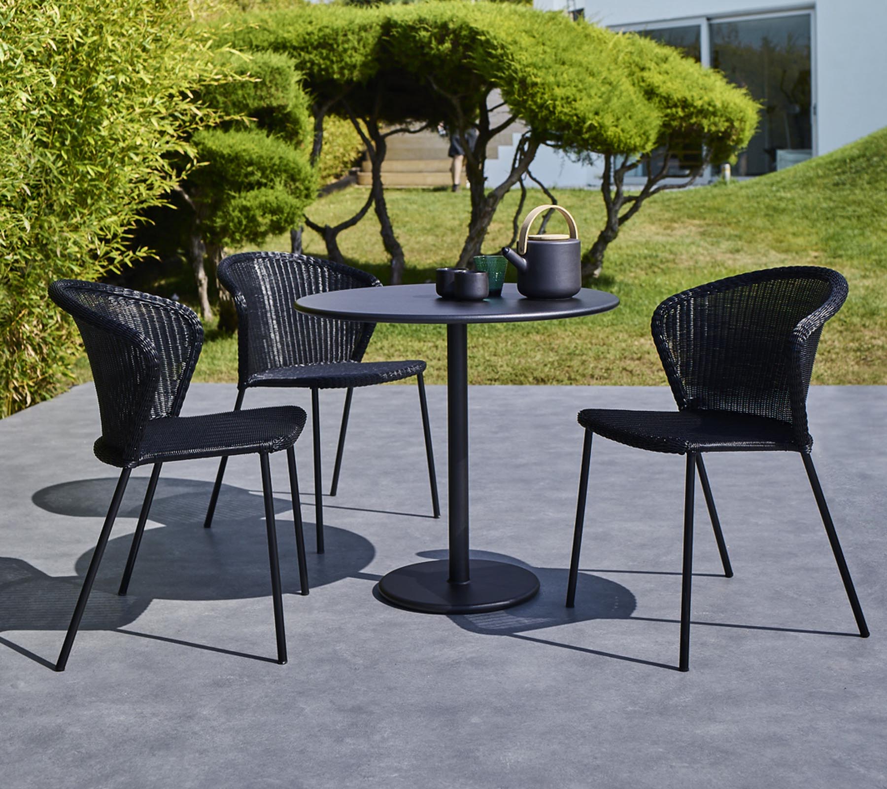 Ein modernes Gartentischset mit einem runden Tisch und drei schwarzen geflochtenen Stühlen, komplett mit einer Teekanne und Tassen auf dem Tisch.