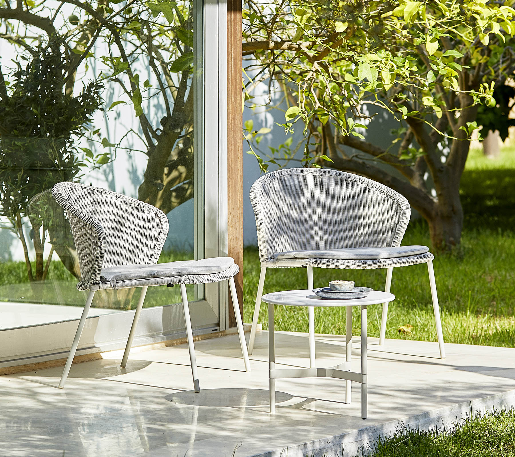 Zwei stilvolle Stühle und ein kleiner Tisch in einer ruhigen Umgebung mit Grünpflanzen, perfekt zum Entspannen und für Outdoor-Veranstaltungen.