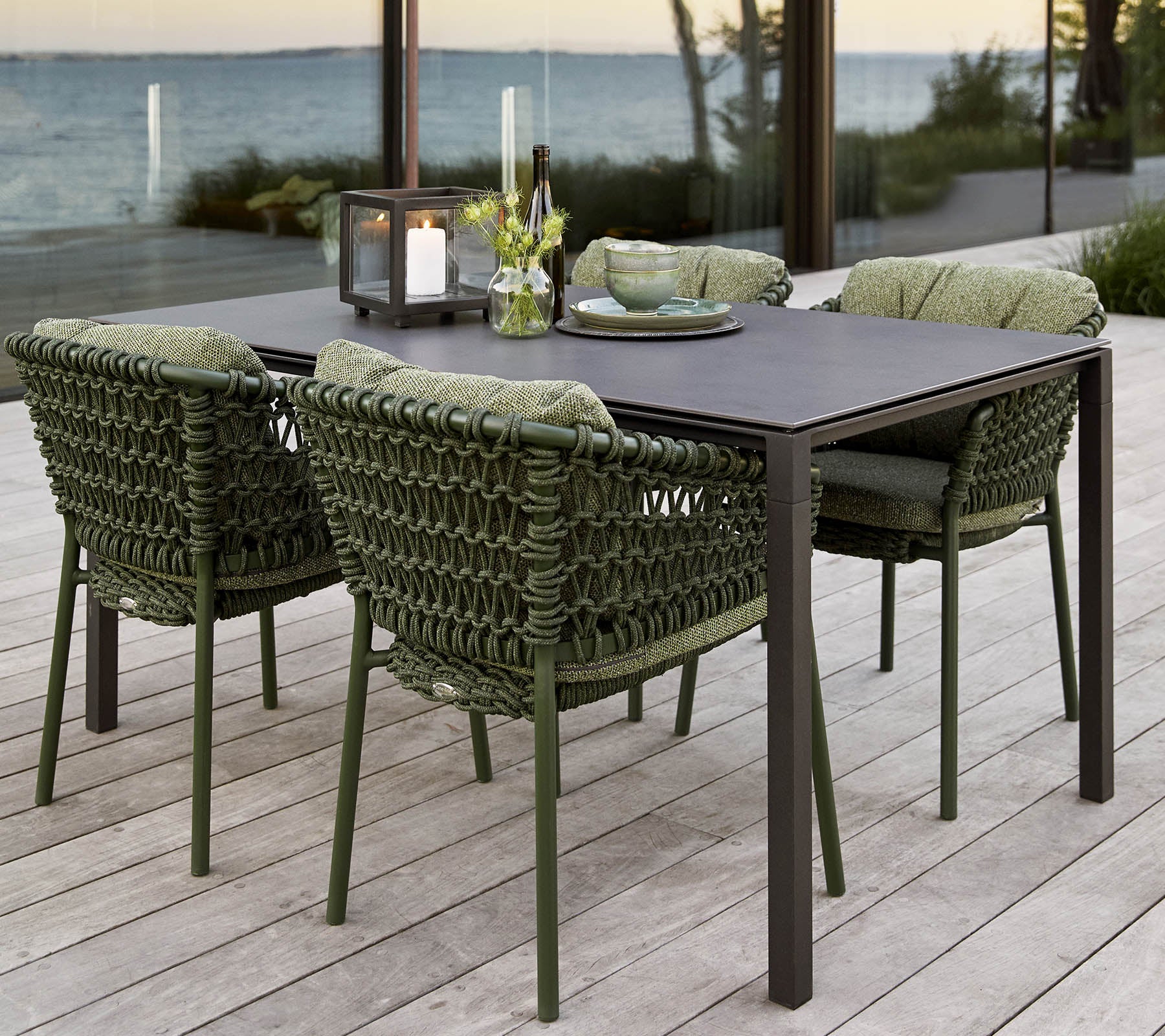 Stylisches Outdoor-Esstisch-Set mit einem rechteckigen Tisch und vier gepolsterten, geflochtenen Stühlen, ergänzt durch ein Blumenarrangement als Mittelstück.