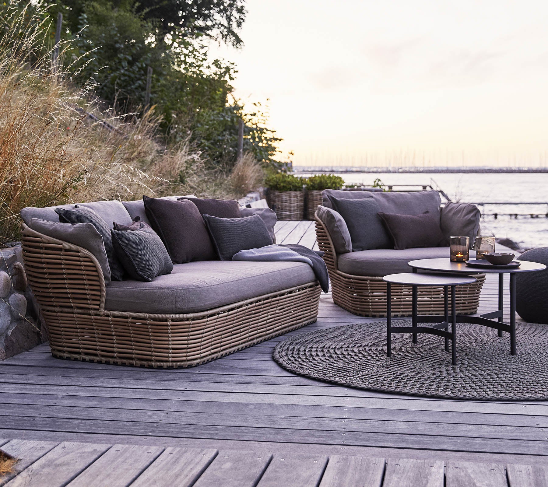 Stylischer Außenbereich mit zwei gepolsterten, geschwungenen Sofas mit dunklen Kissen und einem runden Couchtisch auf einer Holzoberfläche.