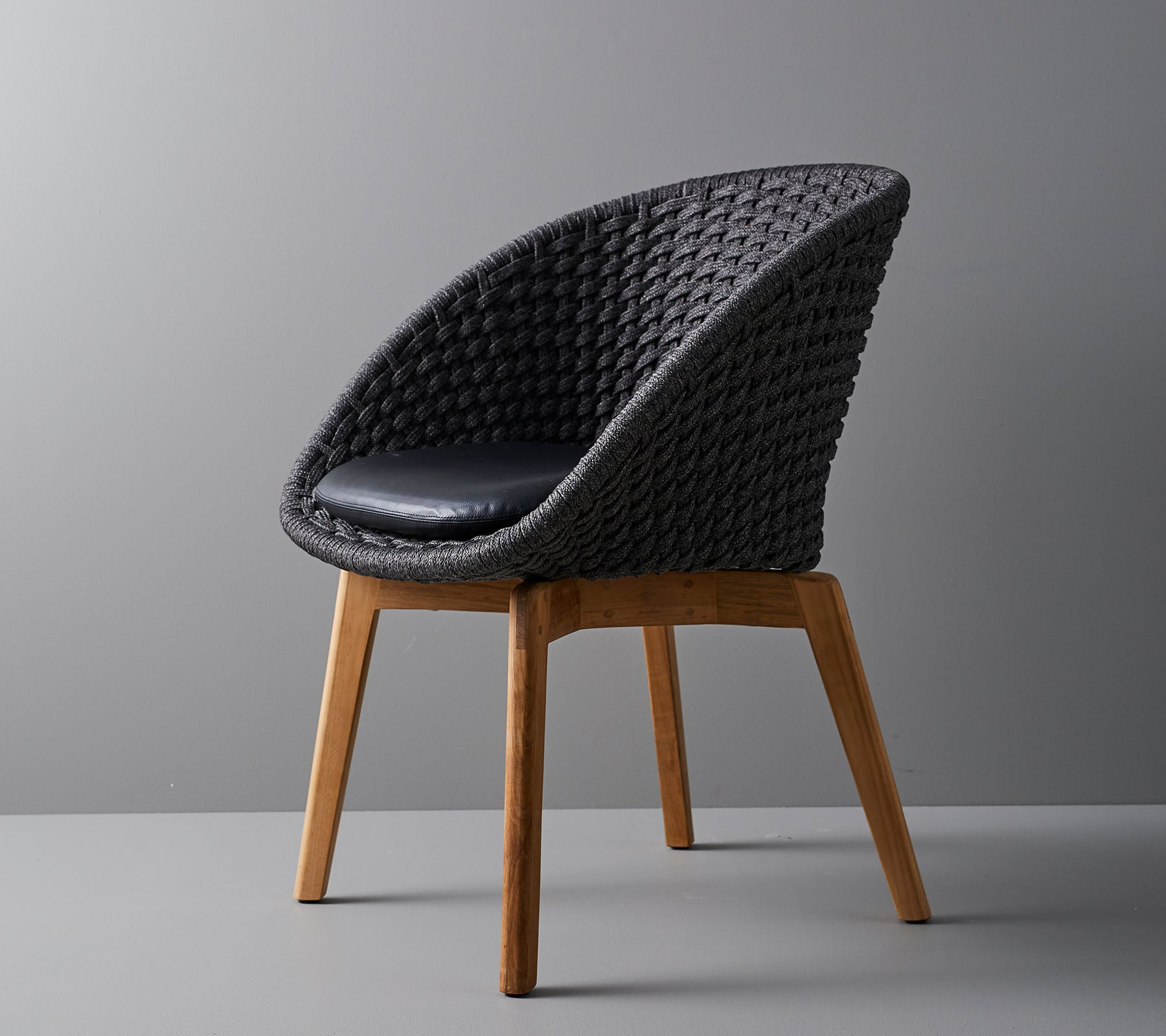 Stilvoller, gewebter Stuhl mit einem bequemen Kissen, ausgestattet mit glatten, konischen Holzbeinen und einem modernen Design, das für verschiedene Umgebungen geeignet ist.