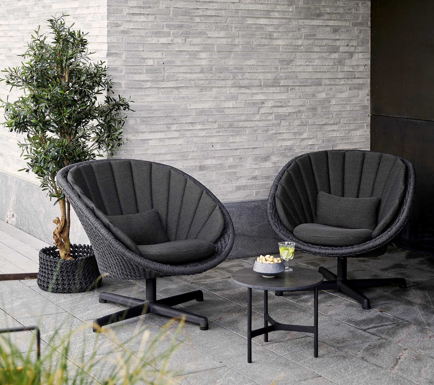 Zwei stilvolle, moderne Stühle mit rundem Design, begleitet von einem kleinen Tisch und einer Topfpflanze, vor einer strukturierten Wand.