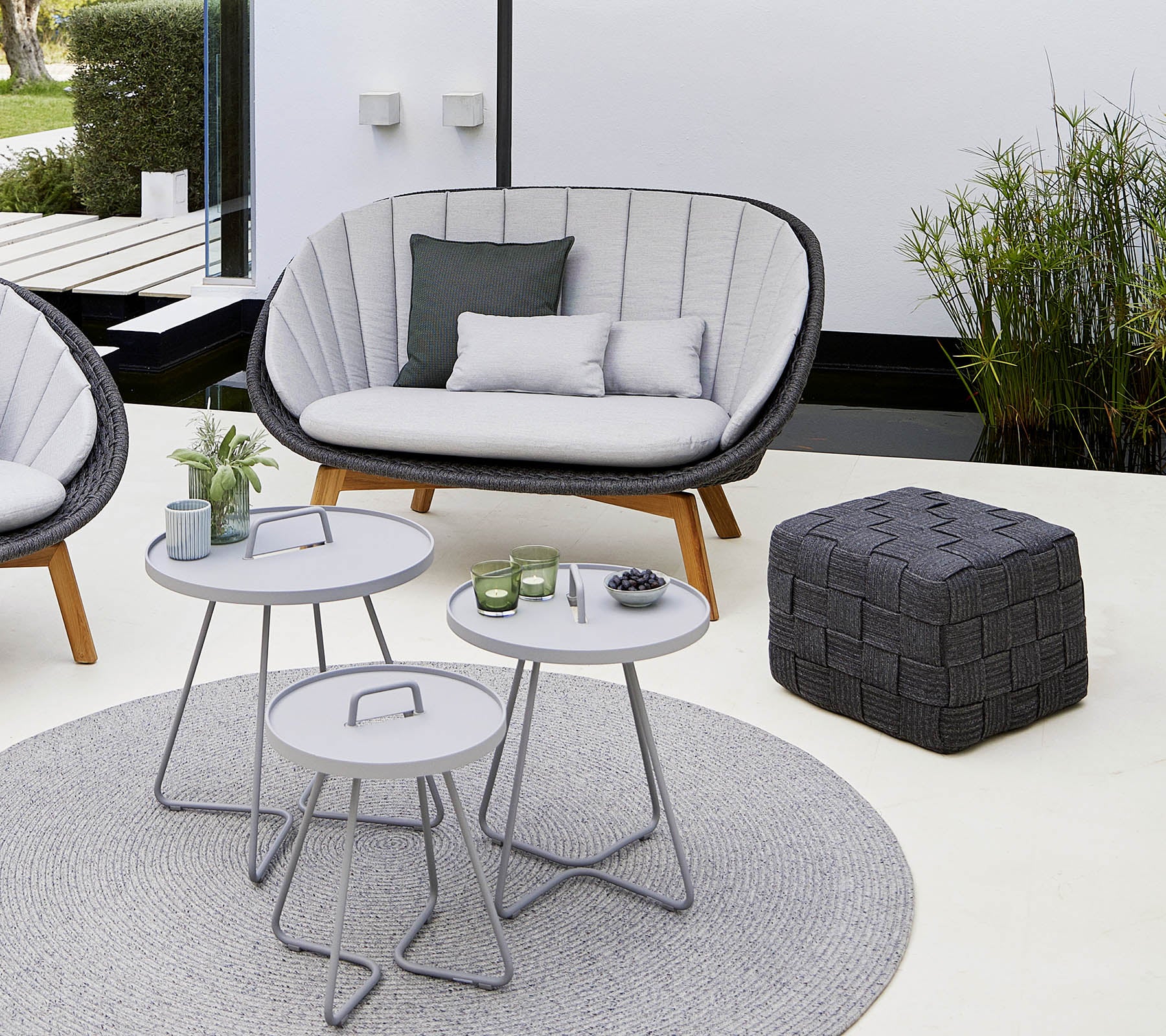 Gemütlicher Sitzbereich mit einem stilvollen Sofa, ein paar runden Tischen, einem dekorativen Pouf und einem weichen Teppich, umgeben von Pflanzen.