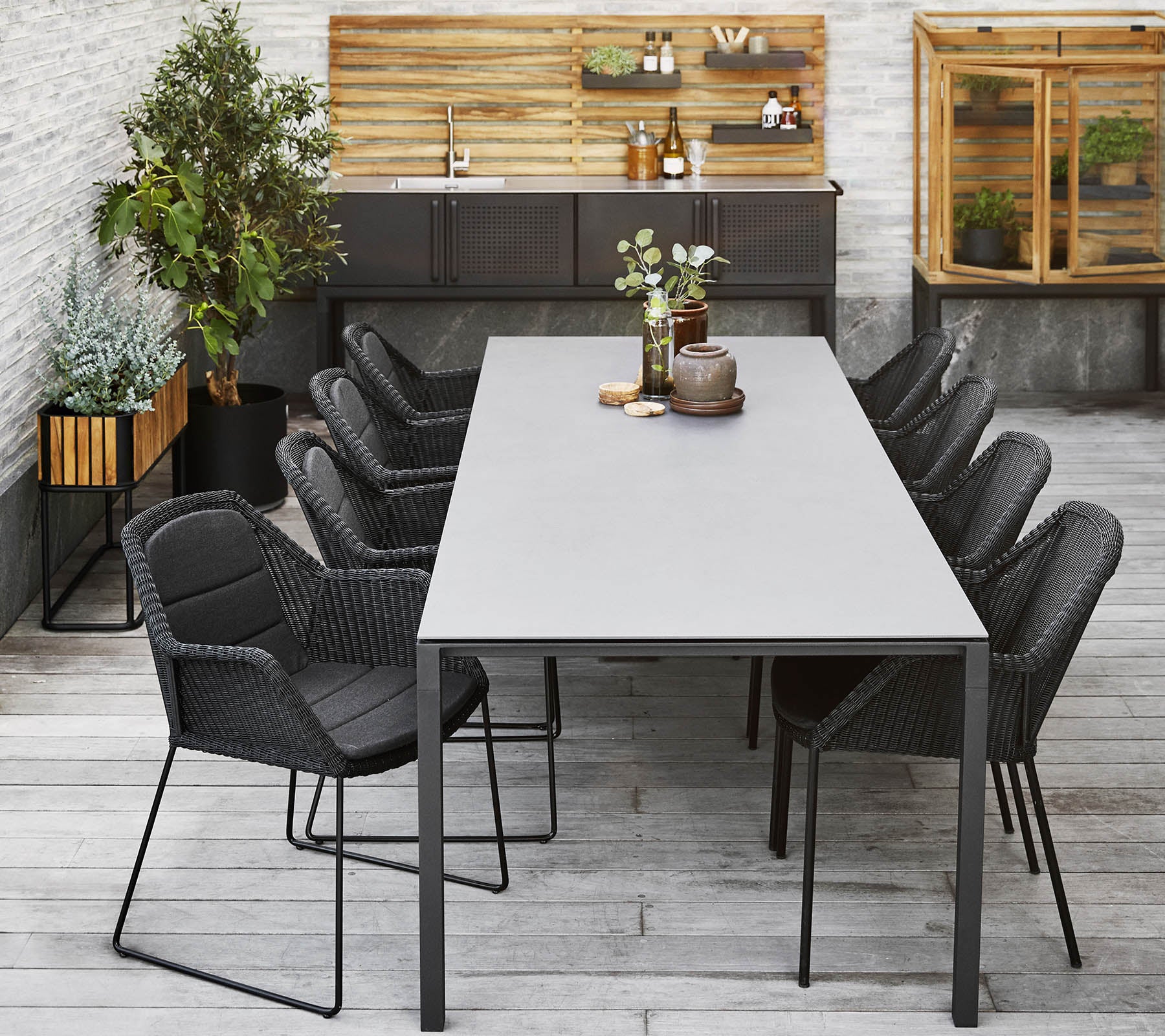 Ein modernes Esszimmer-Setup mit einem langen Tisch, umgeben von schlanken schwarzen Stühlen, ergänzt durch dekorative Pflanzen und eine Holzrückwand.