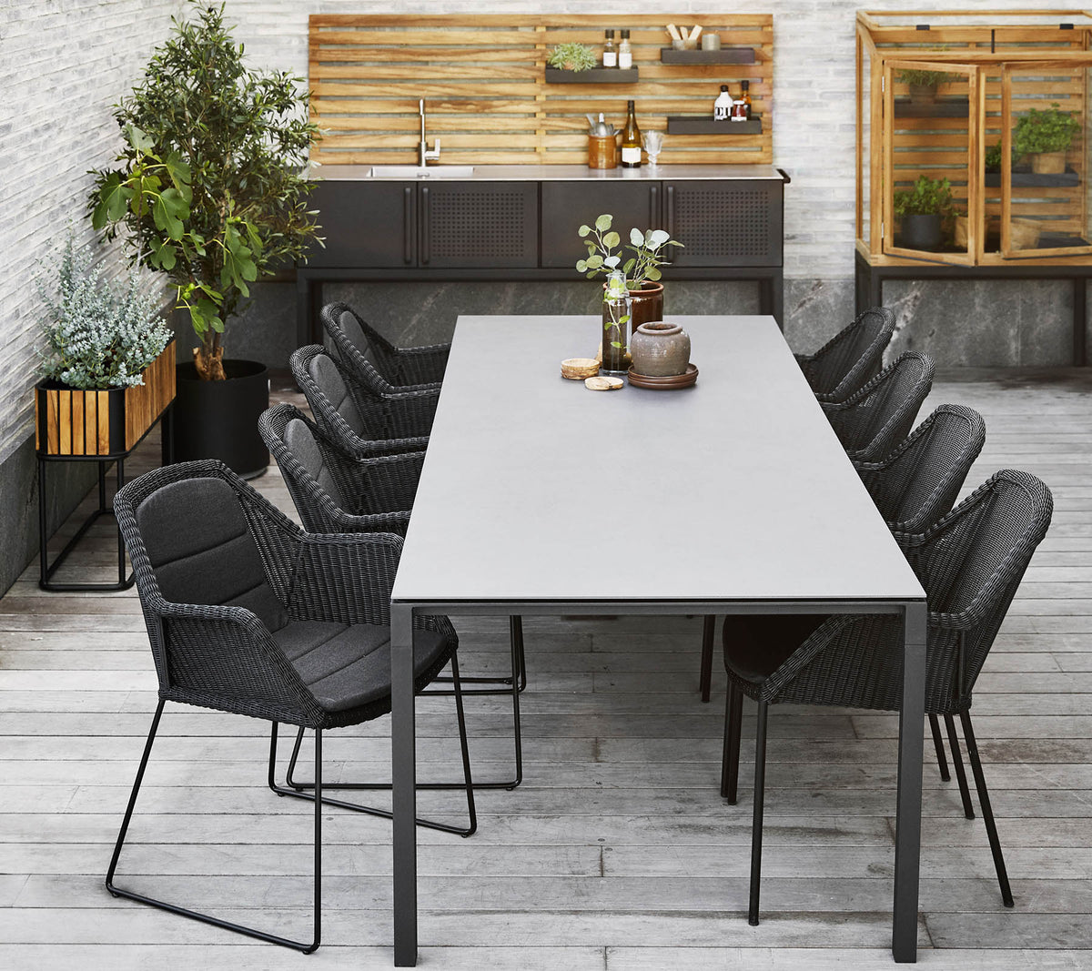 Ein modernes Esszimmer-Setup mit einem langen Tisch, umgeben von schlanken schwarzen Stühlen, ergänzt durch dekorative Pflanzen und eine Holzrückwand.