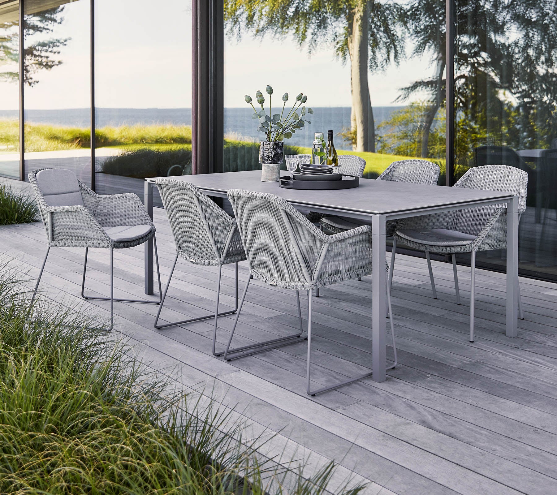 Ein stilvolles Gartentischset mit einem rechteckigen Tisch und sechs geflochtenen Stühlen, umgeben von Grün und einer malerischen Aussicht.