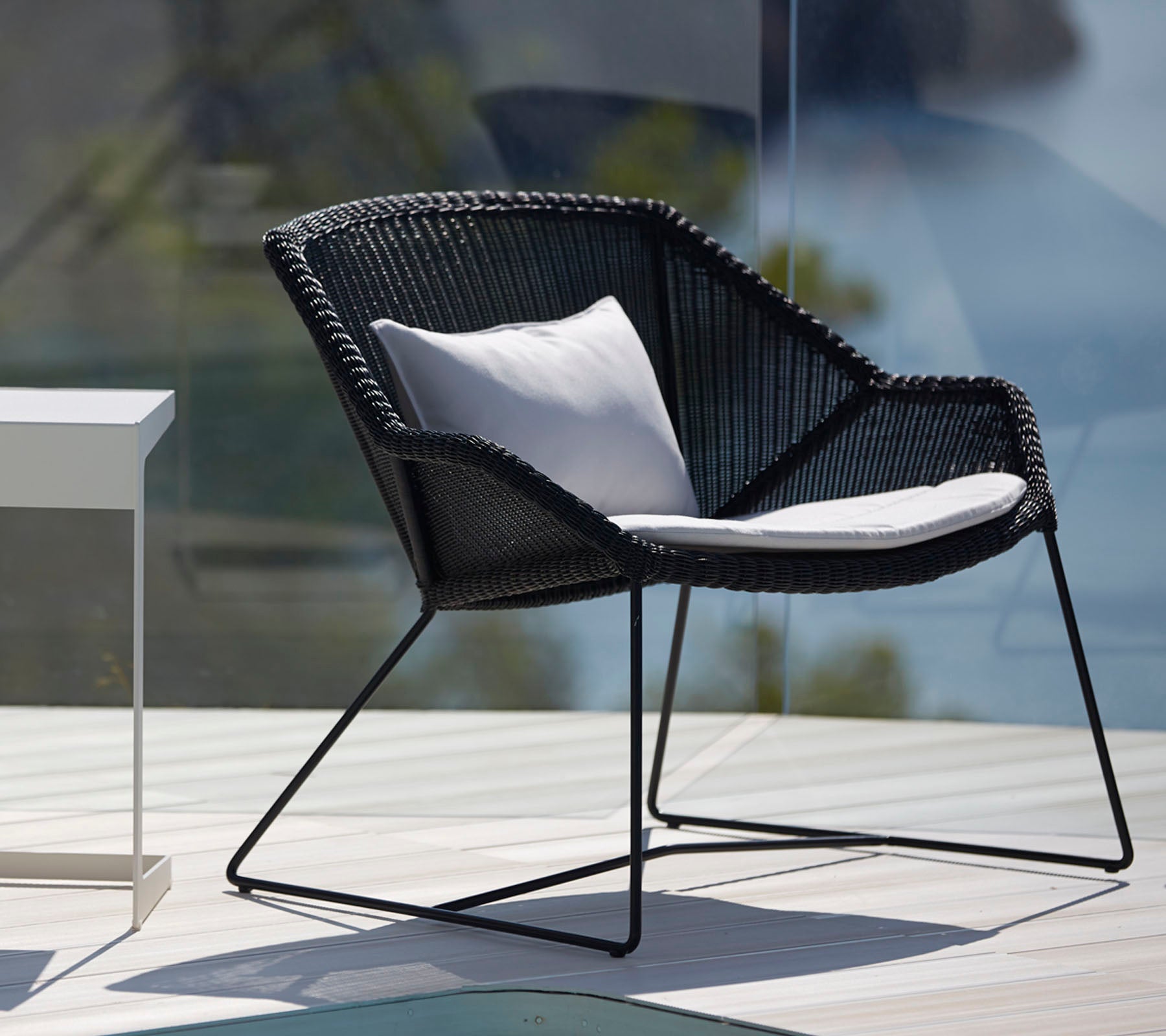 Moderne schwarze Stuhl mit weißem Kissen in einem stilvollen Außenlounge-Setting.
