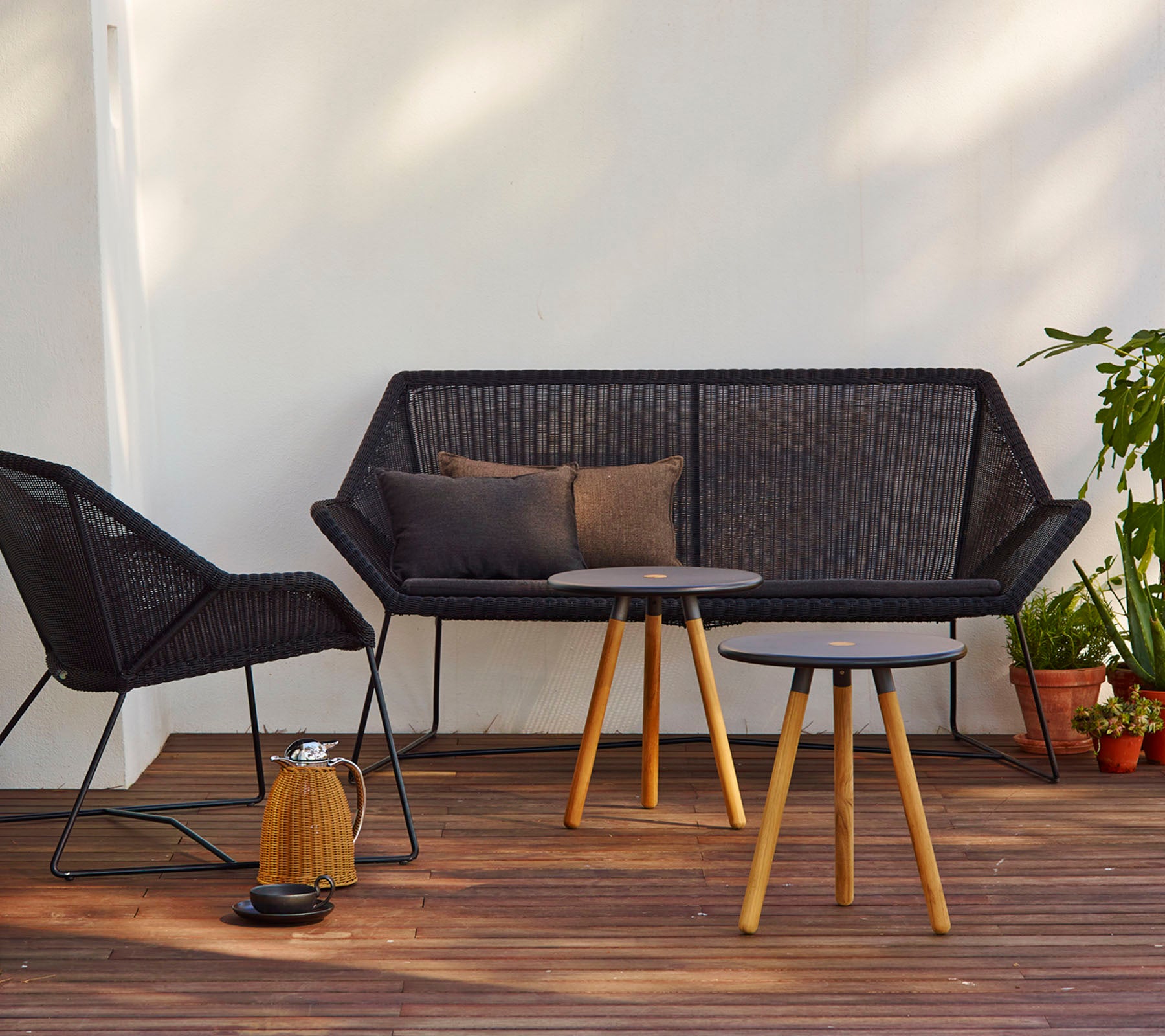 Zeitgemäße Sitzanordnung mit einem schwarzen Sofa mit Kissen, einem passenden Stuhl und einem runden Tisch mit Holzbeinen.
