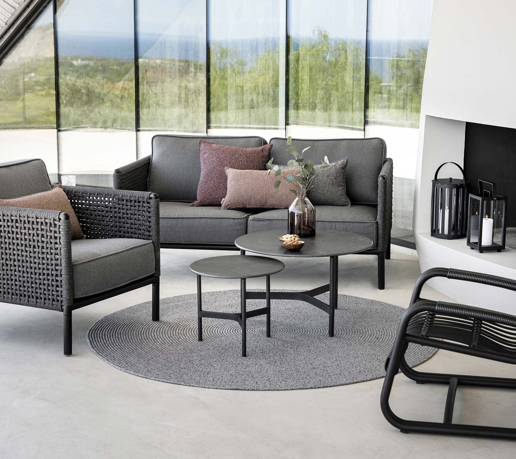 Stylischer Sitzbereich mit einer grauen Couch mit Kissen, einem runden Couchtisch und Akzentstühlen auf einem runden Teppich. Natürliches Licht verbessert die Atmosphäre.