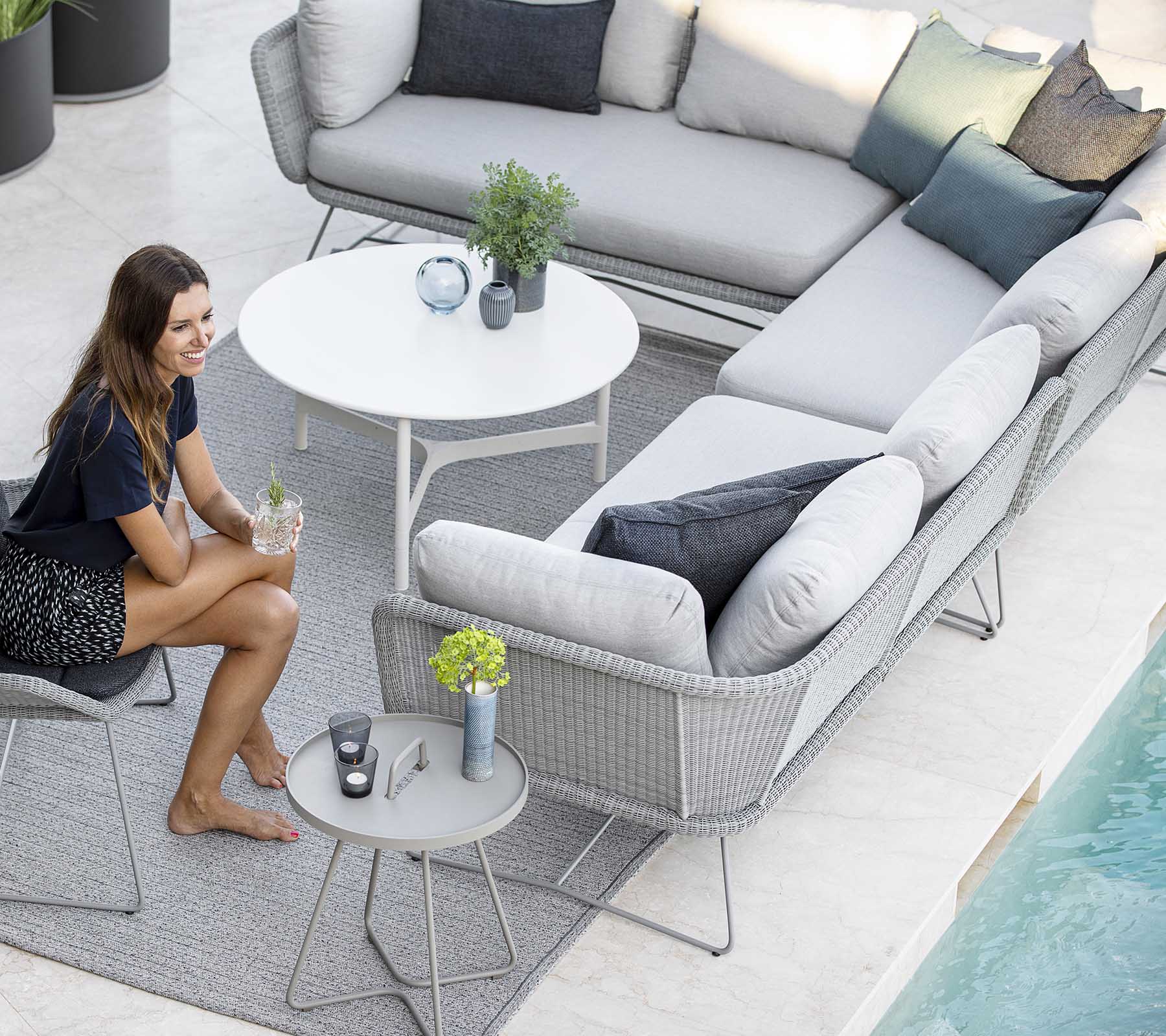 Eine stilvolle Außen-Sitzgelegenheit mit einer Sofa, Akzentkissen und einem kleinen Tisch, ergänzt durch Pflanzen und einen Pool in der Nähe.