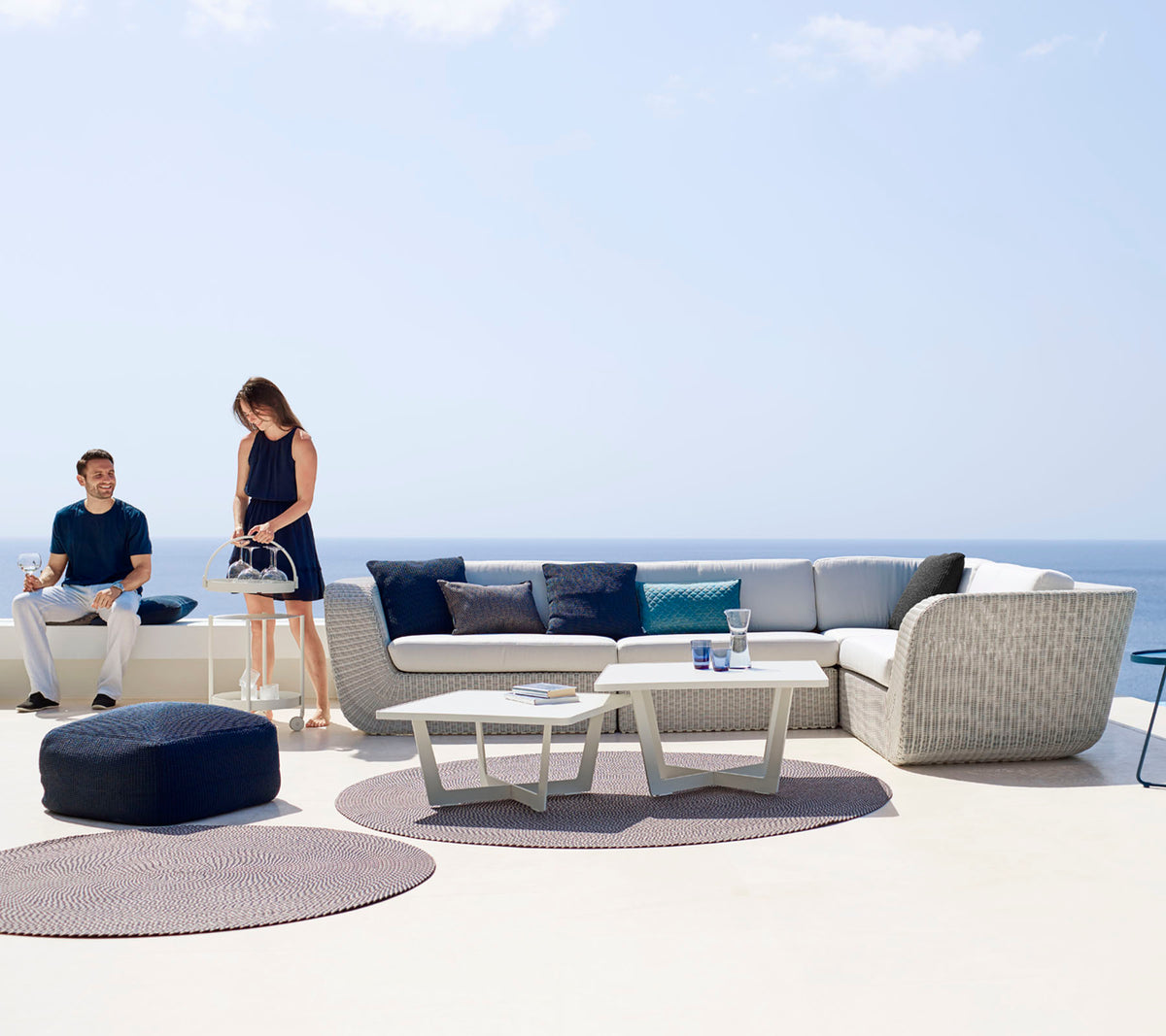 Ein modernes Außenbereich mit einer modularen Sofa, einem Couchtisch und dekorativen Teppichen, wo zwei Personen den Raum genießen.