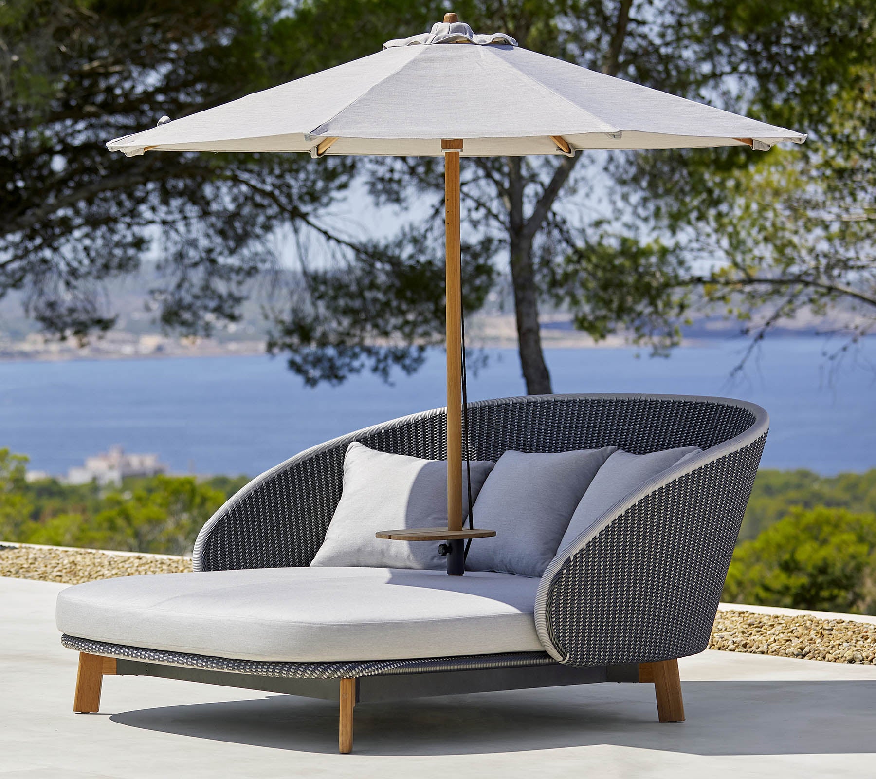 Stylischer Outdoor-Loungesessel mit bequemen Kissen und einem großen Sonnenschirm für Schatten, vor einer malerischen Kulisse.